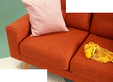 Modern minimalist bir arka plan önünde, turuncu kumaştan yapılmış modern bir kanepe, yumuşak pembe minderler ve dekoratif sarı hasır aksesuarlar yer alıyor.