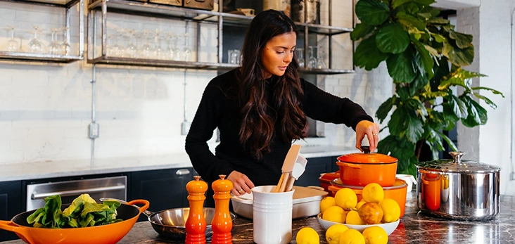 Şık ve modern bir mutfakta, yemek pişirme gereçleri, limonlar ve modern iç tasarım unsurlarıyla çevrili bir kadın yemek hazırlıyor.