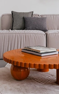 Modern bir oturma odası iç mekanında, nötr tonlardaki yumuşak bir kanepenin önüne, dekoratif kitaplarla süslenmiş modern bir ahşap sehpa yerleştirilmiştir.